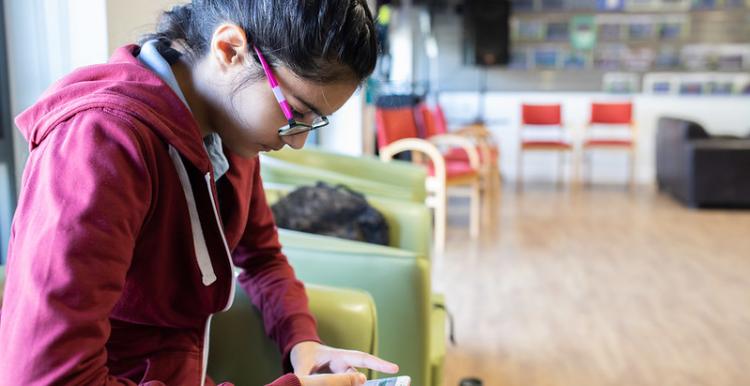 Teenage girl sitting in a cafe looking at her phone.