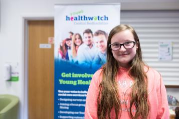 Young girl standing in front of a Healthwatch banner
