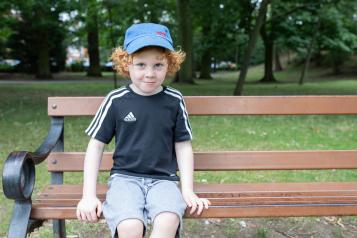 Young boy sitting on a park bench wearing a blue cap