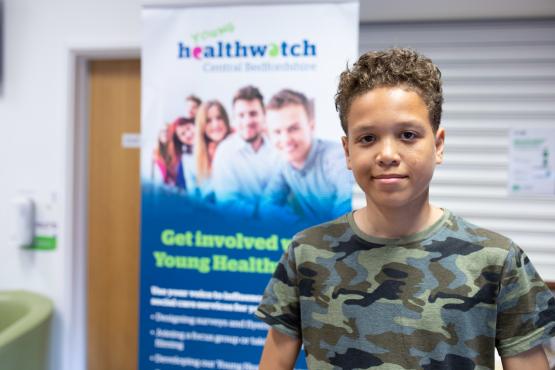 Young boy standing in front of a Healthwatch banner