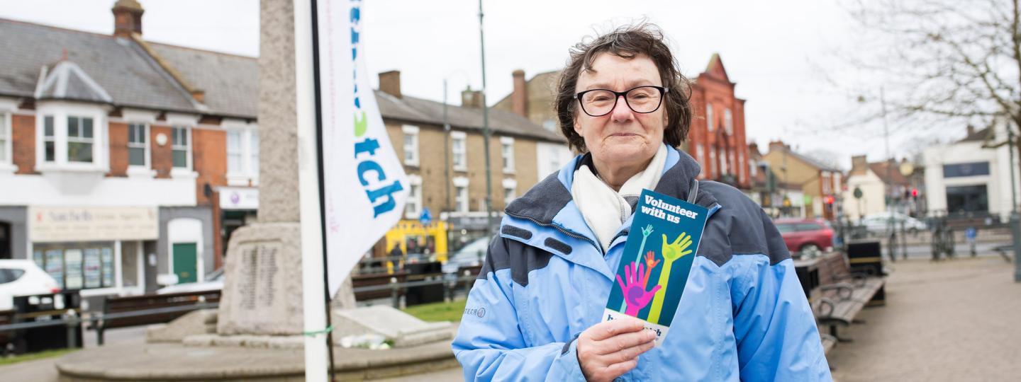 Woman wearing a thick coat and holding a leaflet on volunteering up to the camera