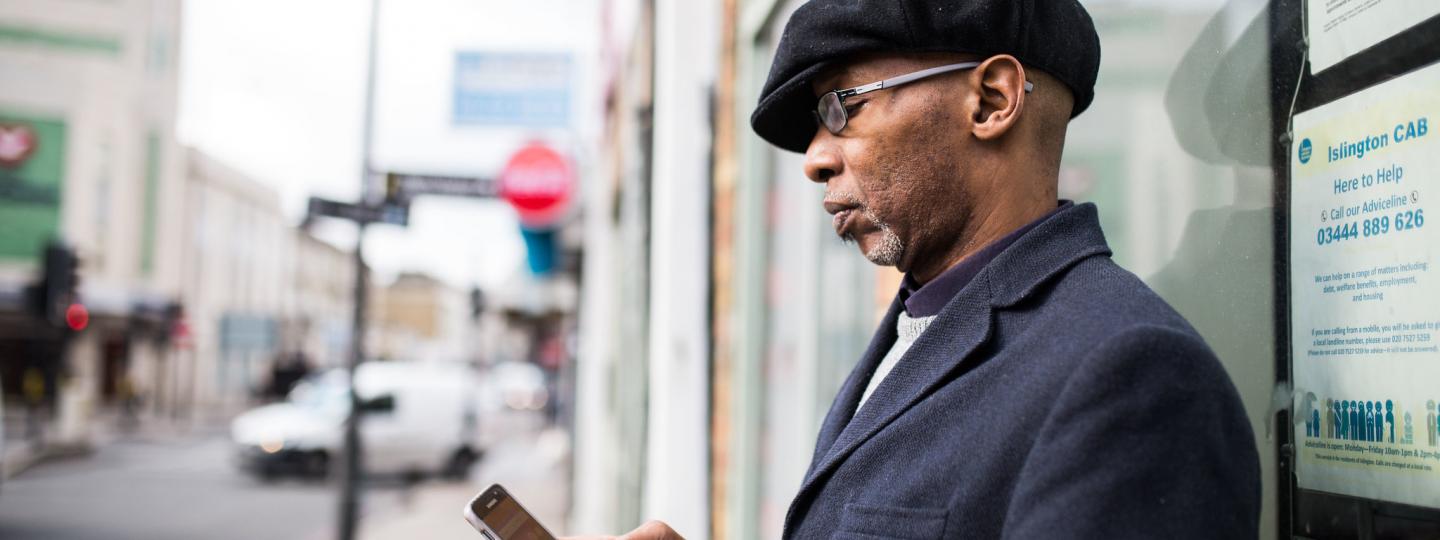 Man wearing a suit leaning on the side of a building and looking at his phone