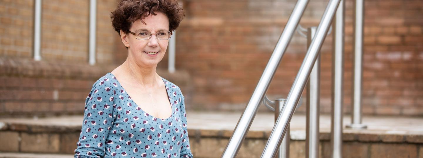 Woman standing at the bottom of some stairs, holding the hand rail