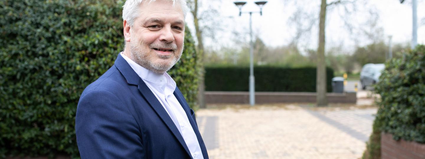 Man wearing a suit standing in front of a hedge smiling at the camera