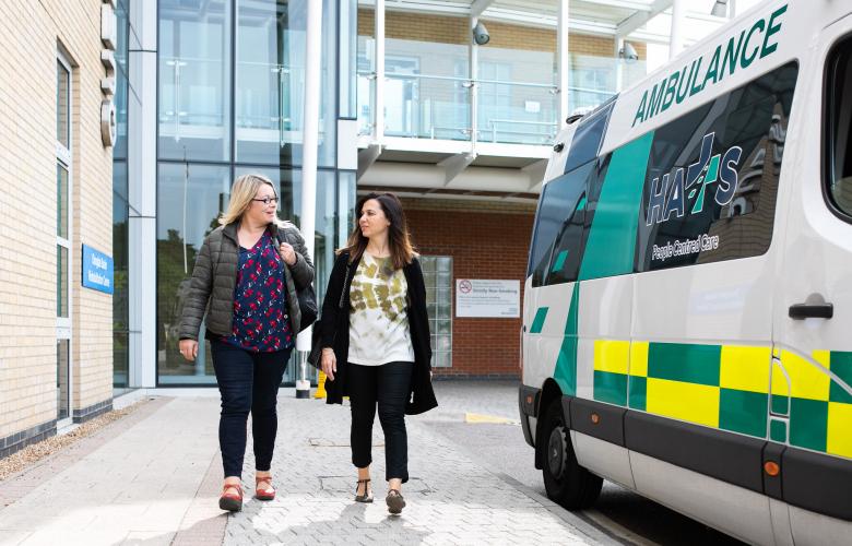 Two women outside a hospital near an ambulance